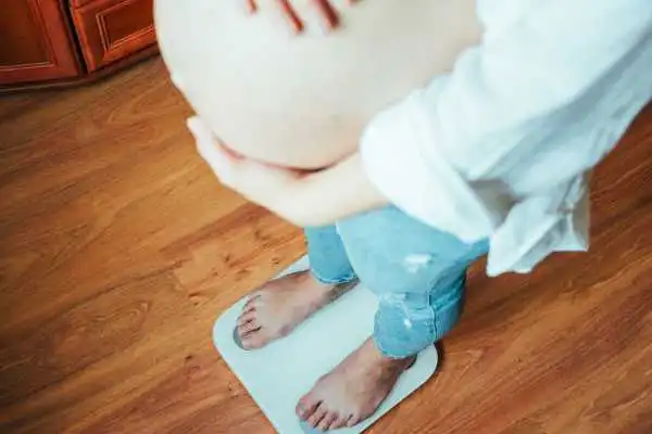 Image of woman weighing herself and experiencing weight gain through pregnancy Uckfield